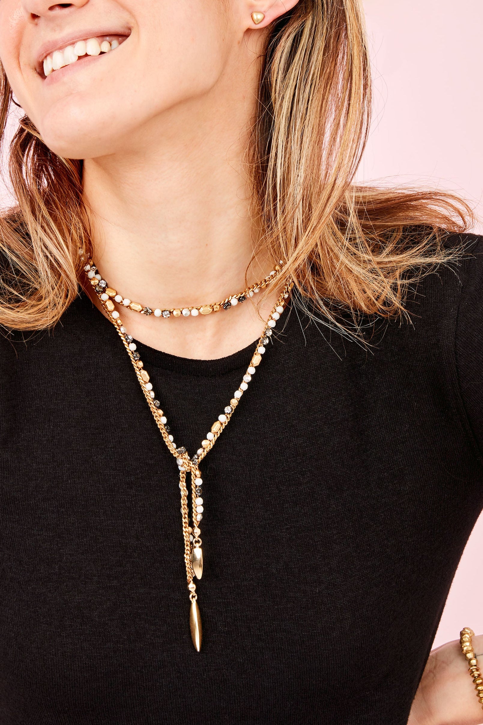 Woman wearing a long gold necklace and bracelet against a pink background